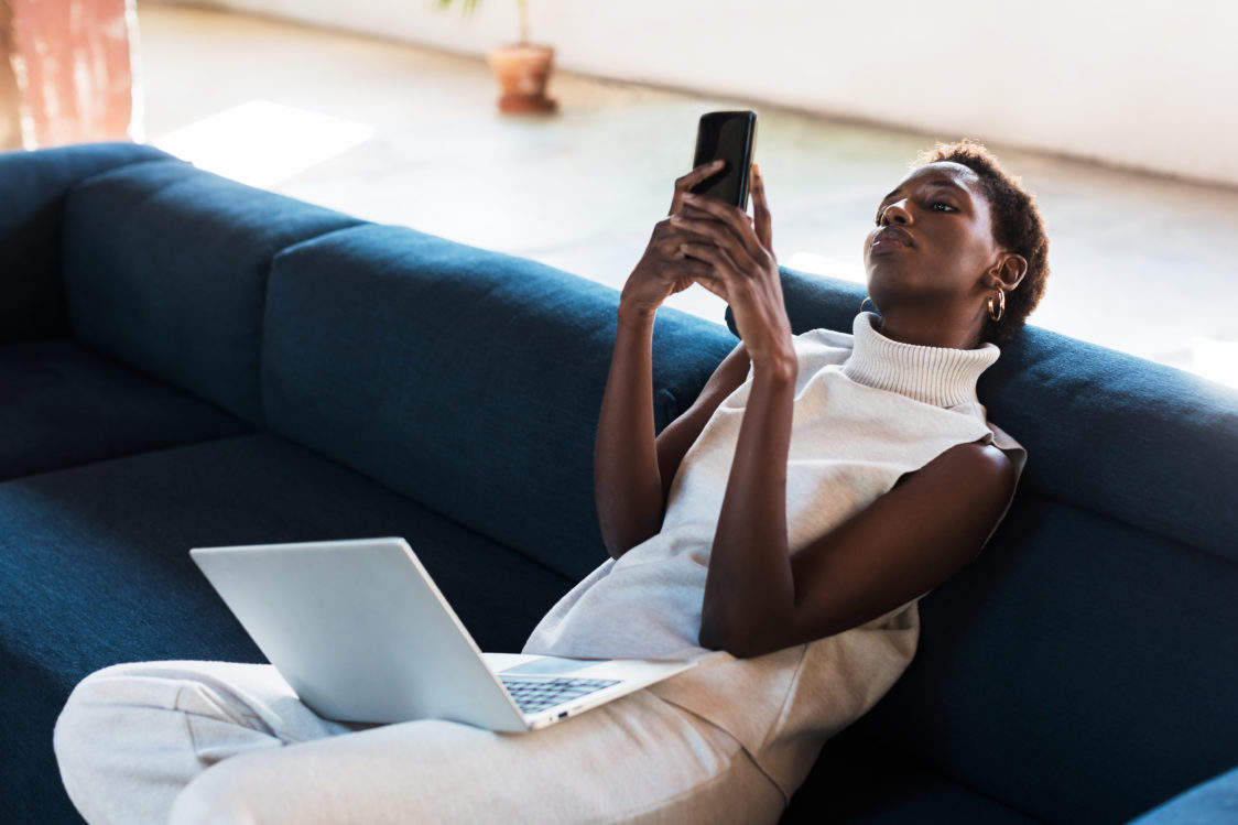 Femme assise sur un canapé qui regarde son téléphone